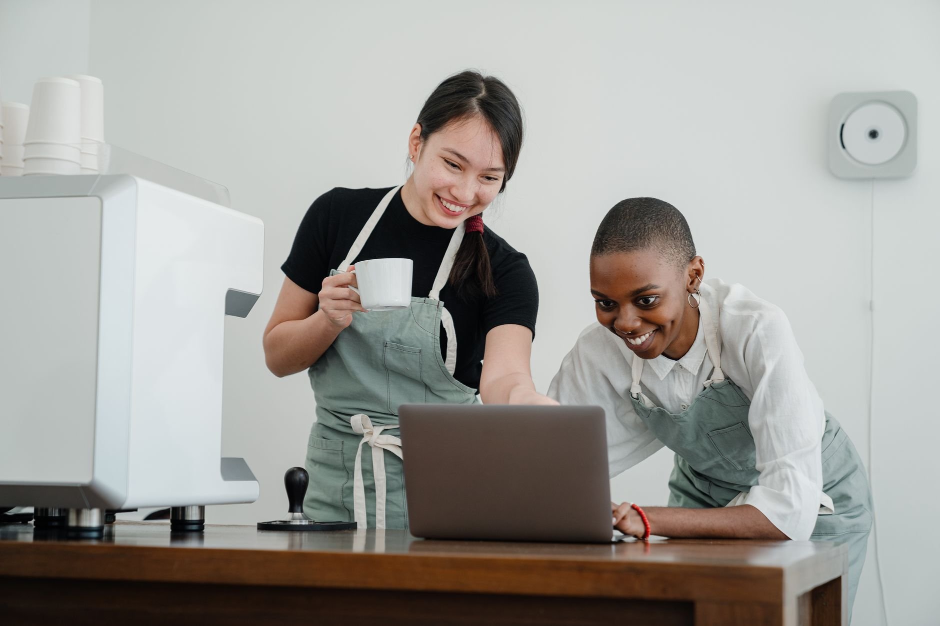 Two people working on a laptop together at a coffee shop, smiling.